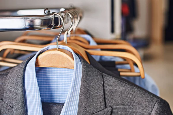 Męskie garnitury i formalne niebieskie koszule na drewnianych wieszaki w sklepie odzieżowego — Zdjęcie stockowe