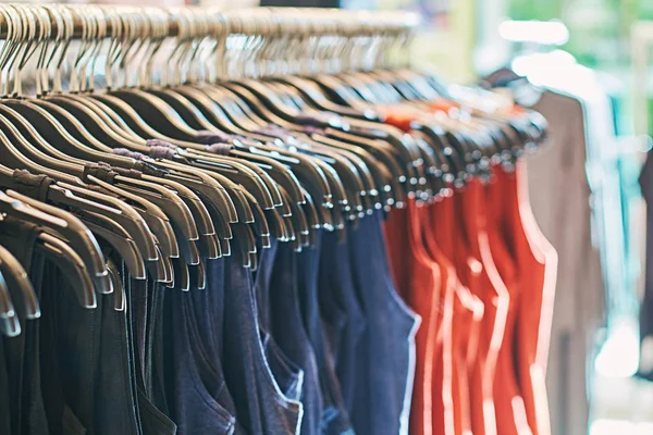 Interior de la tienda de ropa de moda con camisetas en perchas en rojo, azul y otros colores . — Foto de Stock