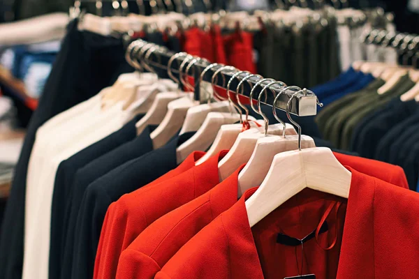 Chaquetas de mujer en rojo, azul, blanco y otros colores en perchas en una tienda de ropa al por menor . — Foto de Stock