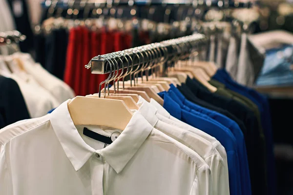 Camisas de mujer en blusas en blanco, azul, negro y otros colores en perchas en una tienda de ropa al por menor . — Foto de Stock