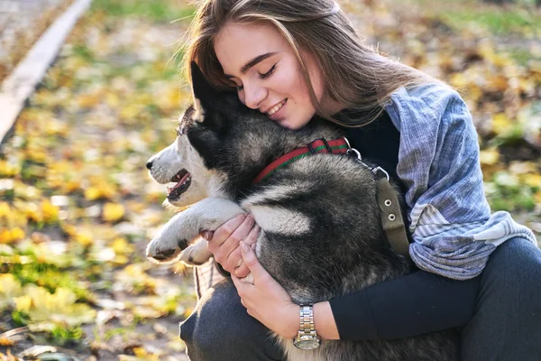 Mladá krásná dívka si zahrává s roztomilým psím psem v podzimním parku pokrytých červenými a žlutými padýma listy — Stock fotografie
