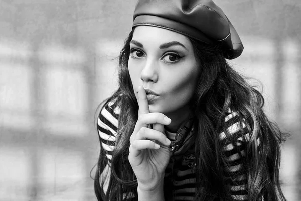 Joven chica morena hermosa vestida en estilo retro vintage en la vieja ciudad europea hace un gesto de silencio en blanco y negro — Foto de Stock
