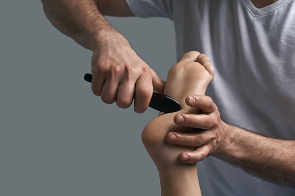 Erkek masör elleri spa salonundaki kadın ayak refleksi bölgesine gua sha kazıma akupunktur aleti kullanarak masaj yapıyor..