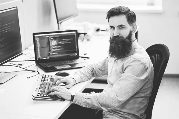 Serious computer programmer developer working in IT office, sitting at desk and coding, working on a project in software development company or startup. Black and white,