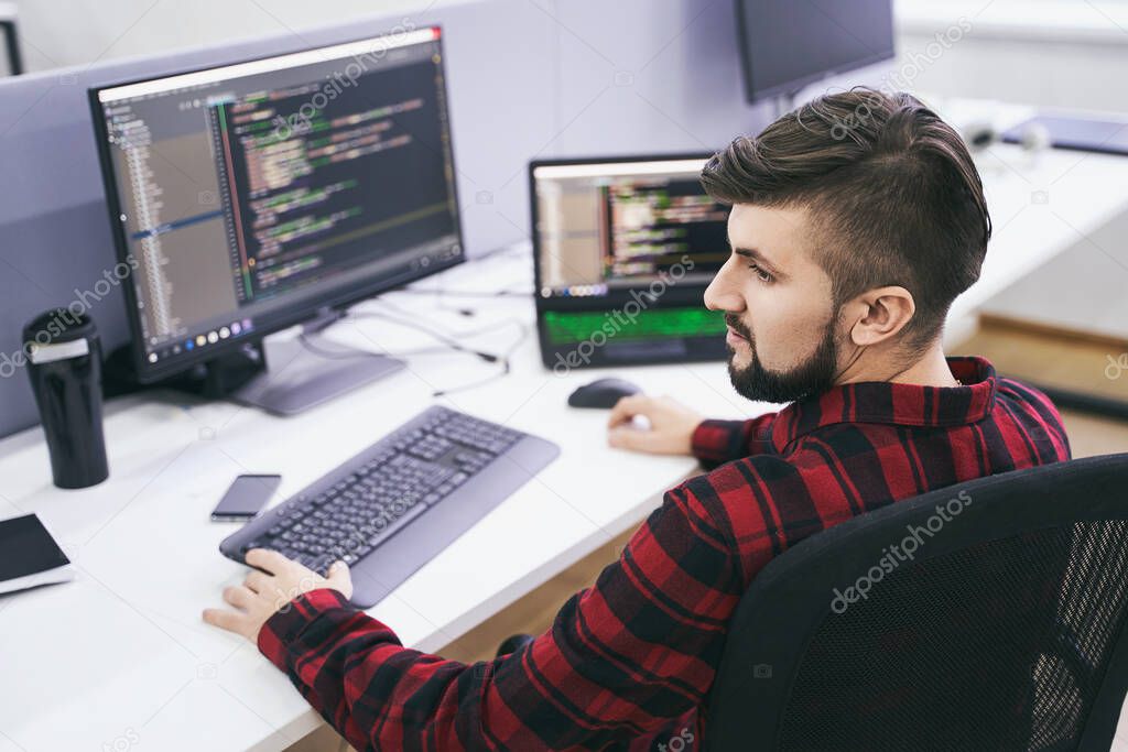 Software developer working on computer in IT office, sitting at desk and coding, working on a project in software development company or technology startup. High quality image.