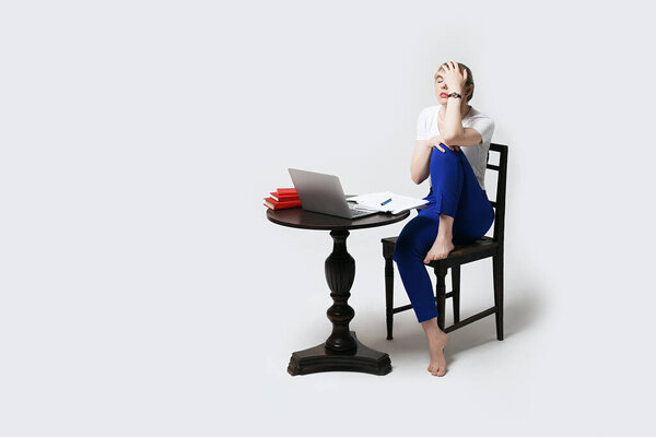 Напряженная молодая студентка, сидящая за столом и работающая или занимающаяся дистанционно в Интернете, делает жест лицевого контакта. Дистанционное обучение или удаленная работа от дома. Изолированный на белом фоне.