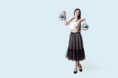 Stüdyoda poz veren esmer, koyu renkli etekli genç bir kız. İki disko topunu tutan kadın ışığı yansıtıyor..