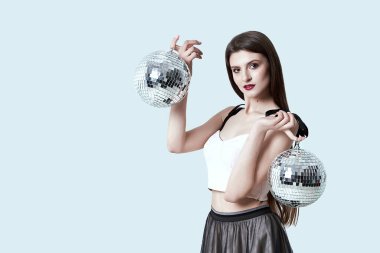 Stüdyoda poz veren güzel esmer kız. İki disko topunu tutan kadın ışığı yansıtıyor..