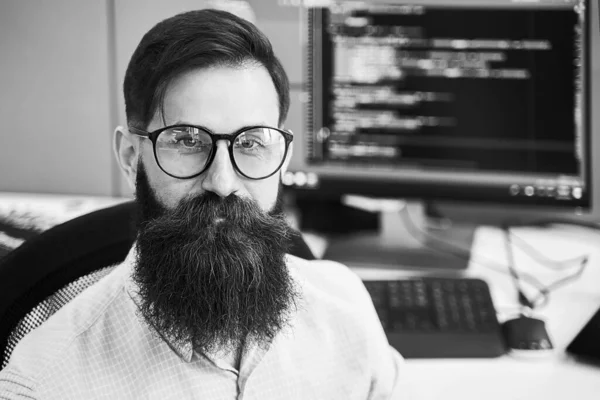 Портрет серйозного розробника комп'ютерних програмістів, який працює в ІТ-офісі, сидить за столом і кодує проект в компанії з розробки програмного забезпечення або стартапі. Чорно-біле. — стокове фото
