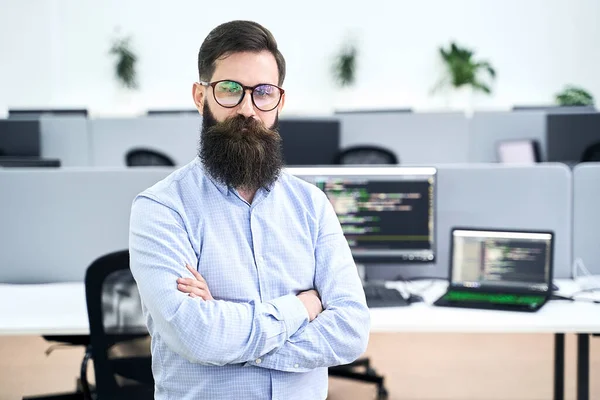 Zelfverzekerde computer programmeur ontwikkelaar staat in IT-kantoor kruising handen op de borst, werken aan een project in software development bedrijf of startup. Hoge kwaliteit imago. — Stockfoto