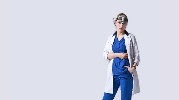 Confiado médico ENT con faros quirúrgicos y gafas protectoras. Retrato del otorrinolaringólogo femenino o cirujano de cabeza y cuello sobre fondo gris claro. — Foto de Stock