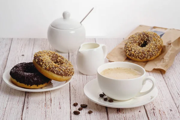 Morning breakfast with chocolate donuts and  cup of coffee with cream on  light wooden background.Delicious donuts sprinkled with crushed nuts.