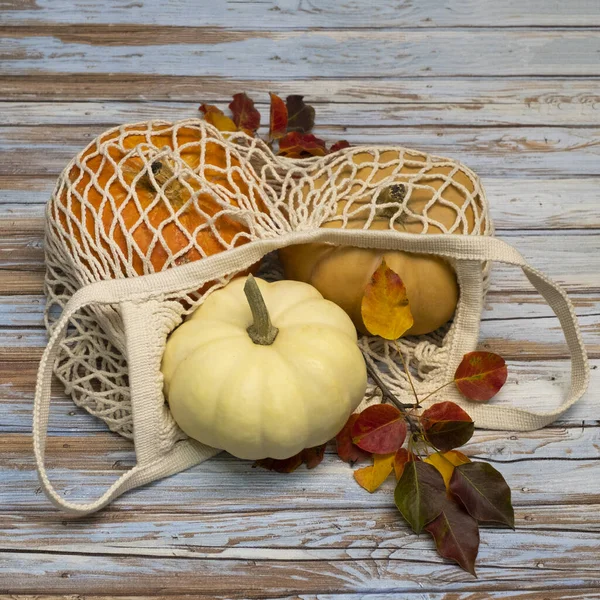 White string bag with pumpkins on an aged wooden background. — Stock Photo, Image