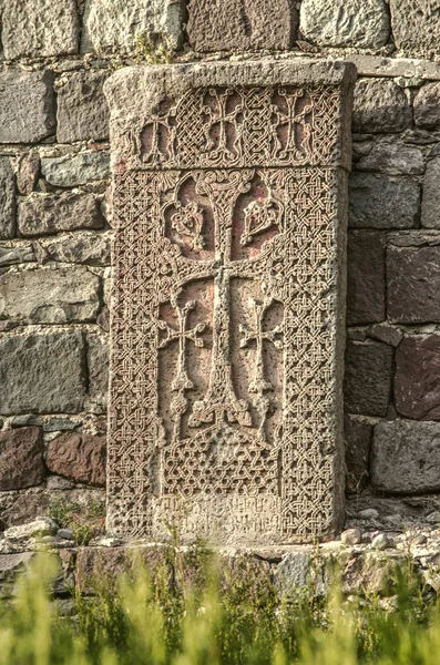 Хачкар стоит у старой стены в парке, расположенном вокруг монастыря Гегард, расположенного в горах Армении — стоковое фото