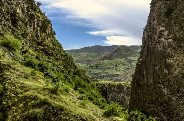 stock image View of the hills in Garni gorge with flowering shrubs and green grass against a blue sky covered with clouds