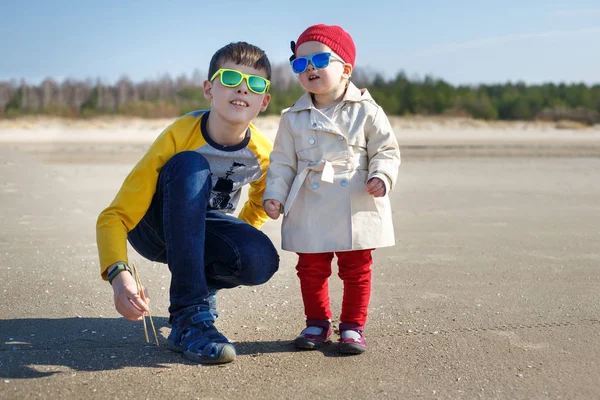 El hermano mayor y su linda hermanita en la playa de primavera en un día soleado. Niños jugando junto al océano — Foto de Stock