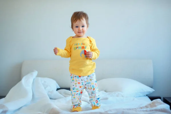 Śmieszne małe dziecko dziewczynę stojącą w łóżku z rodzicami. Niemowlę dziewczynka w piżamie żółty — Zdjęcie stockowe