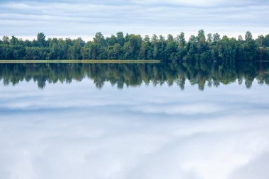 Bir göl, mükemmel yansıma, bulutlar ve orman