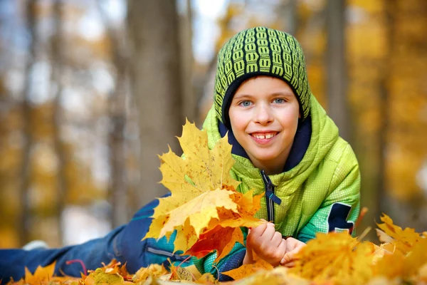 Cheerful little boy lying on the ground in fallen leaves — Stock Photo, Image