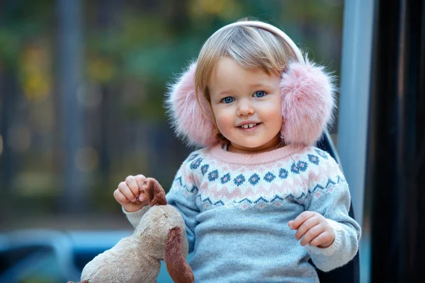 Portret van lief blond klein babymeisje in mooie warme jurk en winter namaakbont oor moffen in Speeltuin — Stockfoto