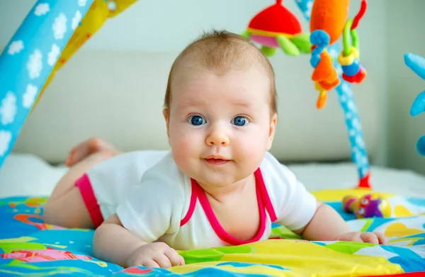 Очаровательная малышка развлекается с игрушками на красочном коврике — стоковое фото
