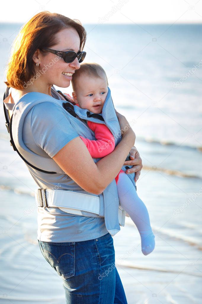 Baby and mother on sea at summer day. Child in a carrier backpack