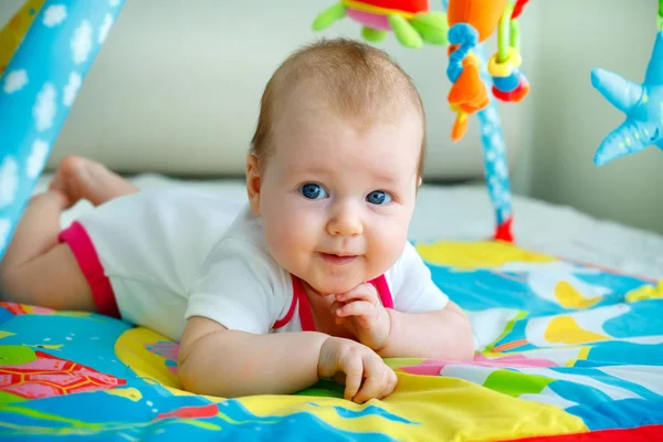 Niña con muchos juguetes coloridos. Pequeño niño acostado en una alfombra de juegos —  Fotos de Stock