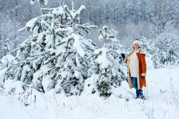 Mujer embarazada joven que usa ropa de abrigo que se divierte en el bosque de invierno — Foto de Stock