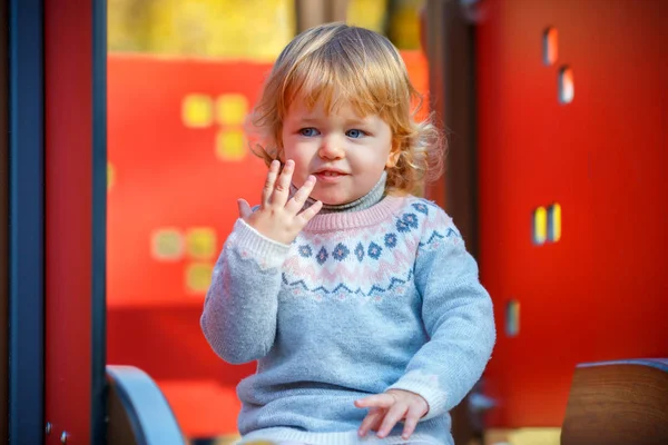 Милая блондинка маленькая девочка в красивом трикотажном платье играет на открытом воздухе на детской площадке — стоковое фото