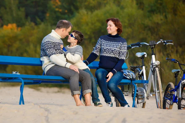 Young family of three having rest on bench during their bike riding on beach — Stock Photo, Image