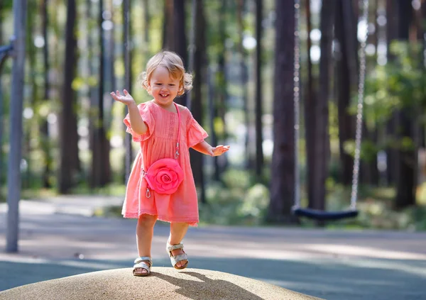 Dulce niña rubia en hermoso vestido de albaricoque juega camina al aire libre en el patio de recreo —  Fotos de Stock