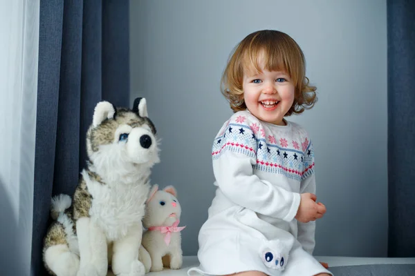 Retrato de niña feliz con el pelo rubio rizado en ropa casual posando en el interior con juguetes para perros y gatos —  Fotos de Stock