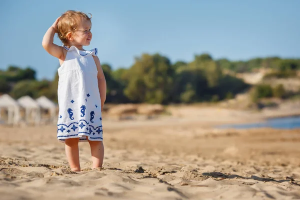 Cute baby kręcone dziewczyna gra na pięknej tropikalnej plaży w białej sukience — Zdjęcie stockowe