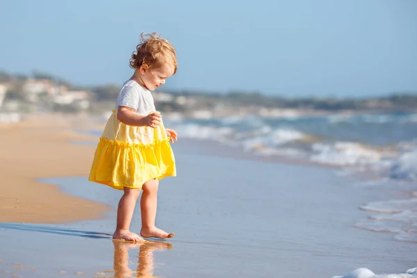Bonito bebê encaracolado menina vestindo um vestido amarelo jogando em uma bela praia tropical — Fotografia de Stock