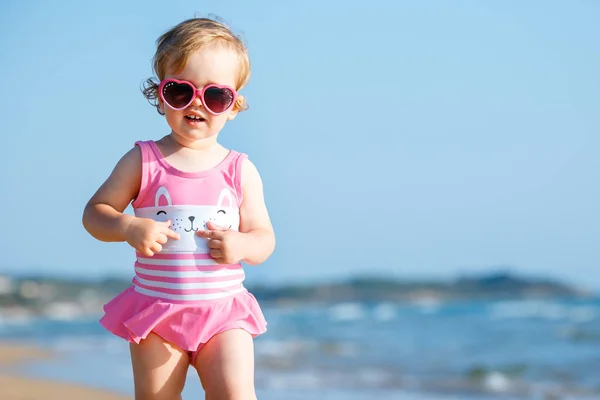 Симпатичная кудрявая девочка, играющая на красивом пляже в симпатичном купальнике — стоковое фото