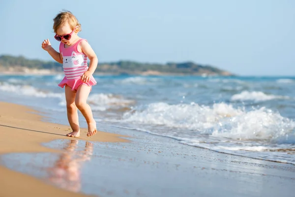 Симпатичная кудрявая девочка, играющая на красивом пляже в симпатичном купальнике — стоковое фото