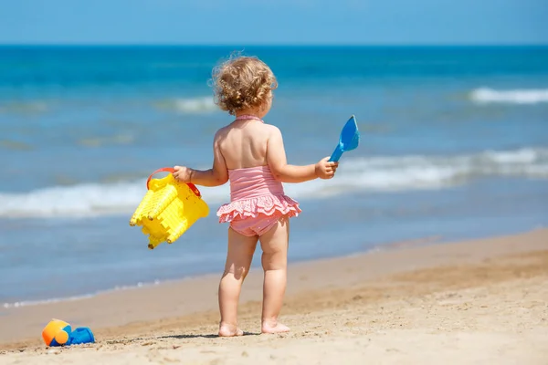Kind spielt am tropischen Strand. kleines Mädchen, das am Meeresufer Sand gräbt. Kinder spielen mit Sandspielzeug. Reisen mit kleinen Kindern — Stockfoto