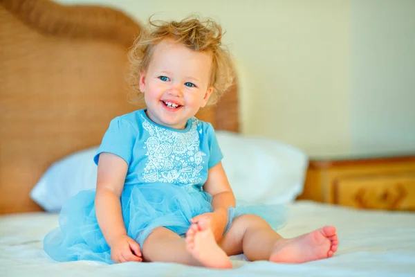 Hermosa niña rubia feliz niño sentado en una cama —  Fotos de Stock