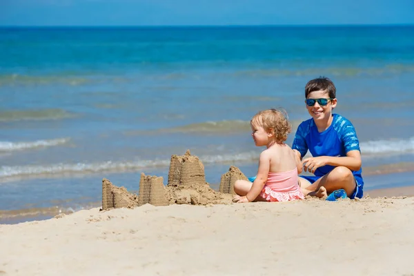 Niños jugando en una playa. Dos niños construyen un castillo de arena en la orilla del mar. Vacaciones familiares en un resort tropical. Viajar con un niño pequeño . — Foto de Stock