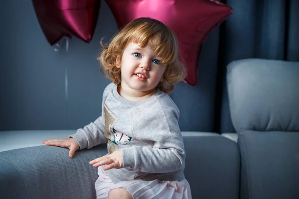 Retrato de menina feliz com cabelo loiro encaracolado em roupas casuais posando dentro de casa com balões estrela no fundo — Fotografia de Stock