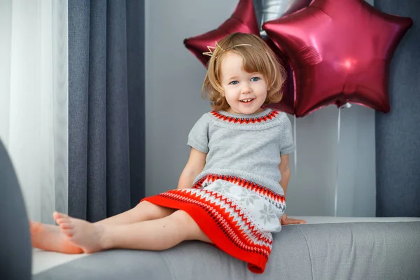 Retrato de niña feliz con el pelo rubio rizado y corona en ropa casual posando en el interior con globos de estrellas en el fondo —  Fotos de Stock