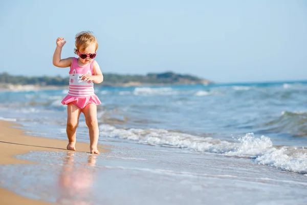 Roztomilá kudrnatá holčička hraje na krásné tropické pláži nosí roztomilé plavky — Stock fotografie
