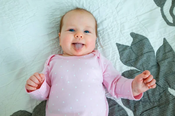 Ευτυχισμένο μωρό κορίτσι στο ροζ κορμάκι ξαπλωμένη ανάσκελα στην κουβέρτα και δείχνοντας τη γλώσσα της — Φωτογραφία Αρχείου