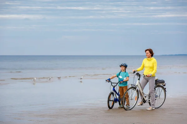 ビーチで自転車に乗る彼女の幼い息子を持つ若い母親 — ストック写真