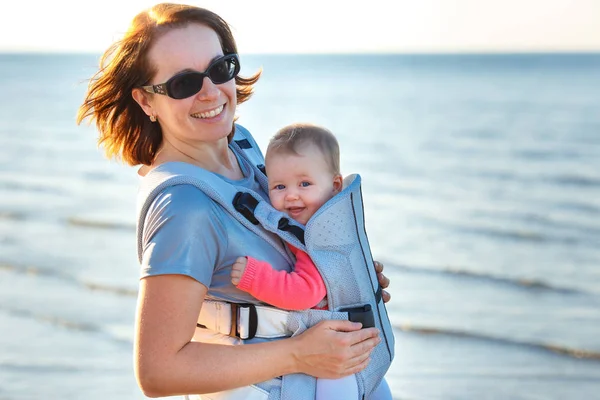 Dziecko i matka na morze w letni dzień. Dziecko w plecaku przewoźnika — Zdjęcie stockowe