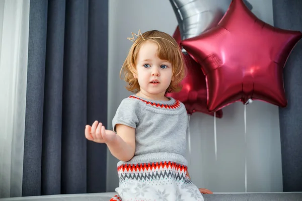 Portrait de heureuse petite fille avec des cheveux blonds bouclés dans des vêtements décontractés posant à l'intérieur avec des ballons étoiles sur le fond Images De Stock Libres De Droits