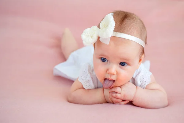 Portrait of a cute newborn baby girl in white dress and hairband lying on her stomach — Stock Photo, Image