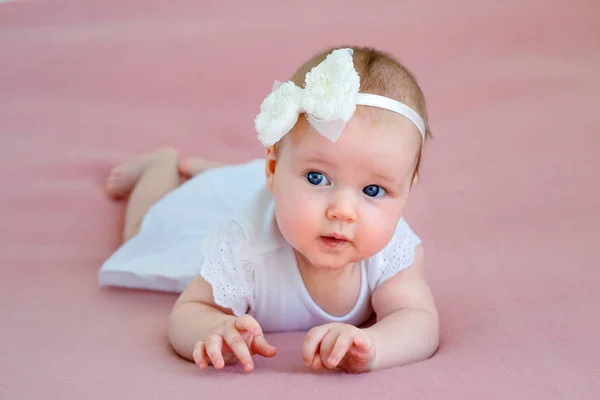 Retrato de um bebê recém-nascido bonito menina em vestido branco e faixa de cabelo deitado em seu estômago — Fotografia de Stock