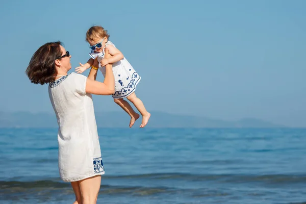 Ung mamma och hennes söta lilla baby flicka spela på en vacker tropisk strand — Stockfoto