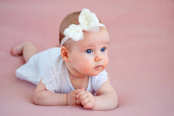 Beyaz elbise ve saç bandı midesinde yatan sevimli bir yenidoğan kız bebek portresi - Stok İmaj